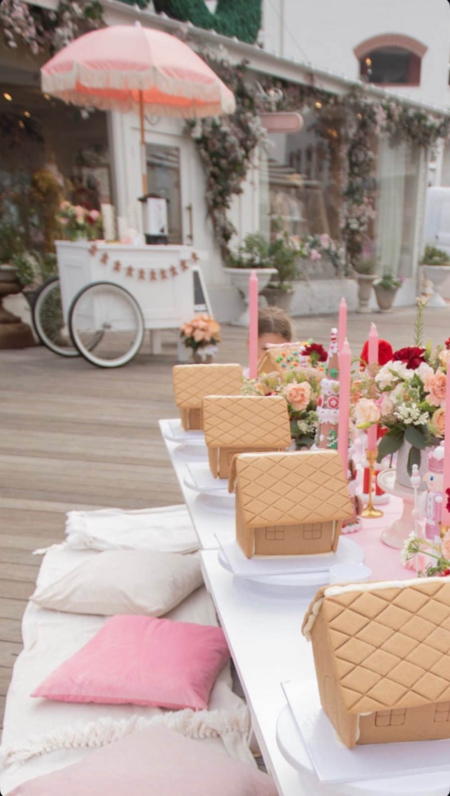 Pink gingerbread party table with gingerbread houses, pink tapers and a cocoa cart
